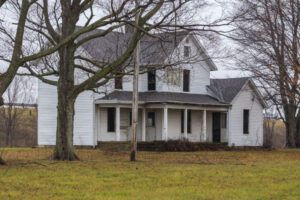 Abandoned house behind barren tree on overcast day